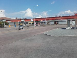En nästan tom parkeringsplats framför en låg byggnad med affärer.